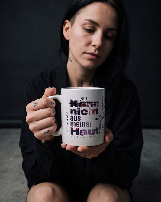Frau sitzt im Studio und hält die Kann nicht aus meiner Haut Tasse mit beiden Händen