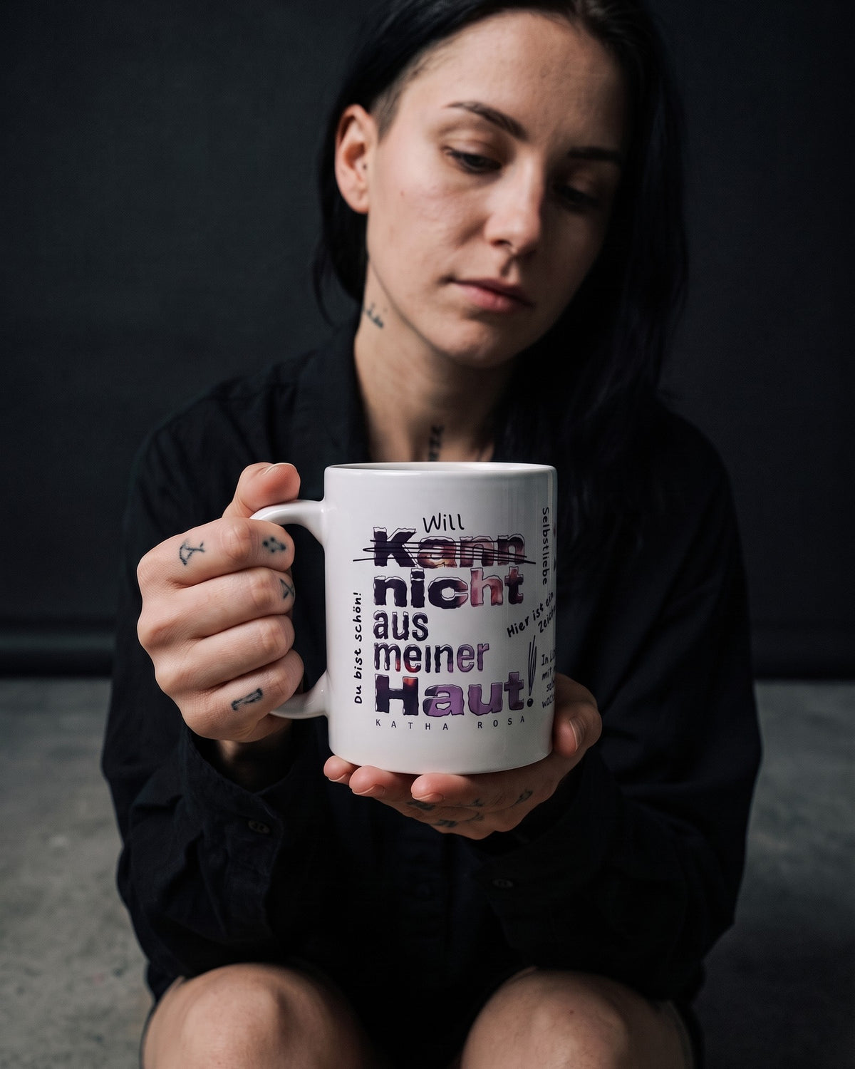 Frau sitzt im Studio und hält die Kann nicht aus meiner Haut Tasse mit beiden Händen